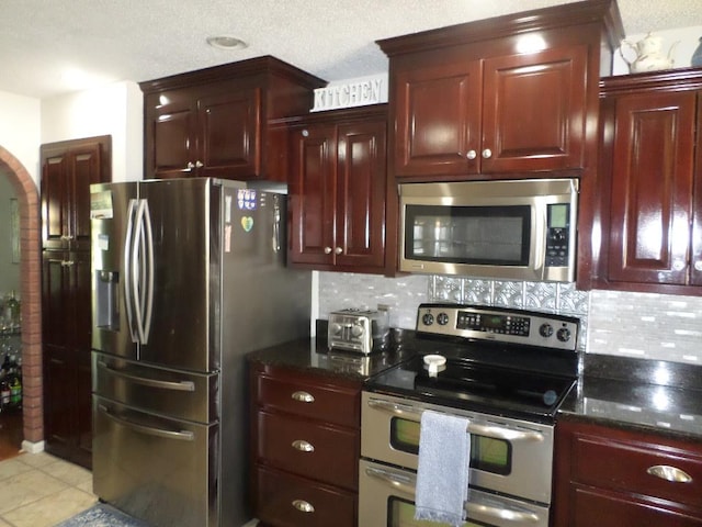 kitchen featuring tasteful backsplash, reddish brown cabinets, dark stone counters, stainless steel appliances, and light tile patterned flooring
