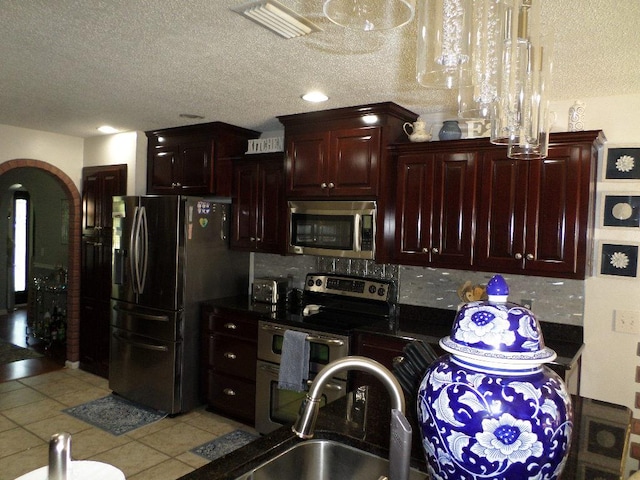 kitchen with a textured ceiling, arched walkways, a sink, light tile patterned floors, and stainless steel appliances