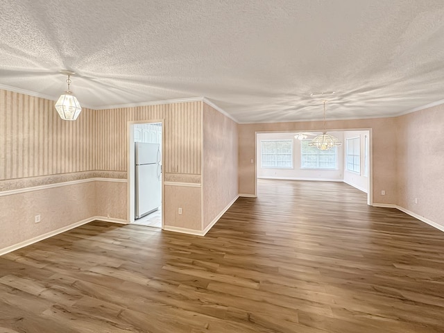 empty room with a chandelier, a textured ceiling, dark hardwood / wood-style flooring, and ornamental molding