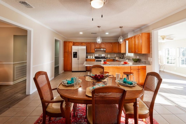 dining area featuring light tile patterned floors, visible vents, ceiling fan, a textured ceiling, and crown molding