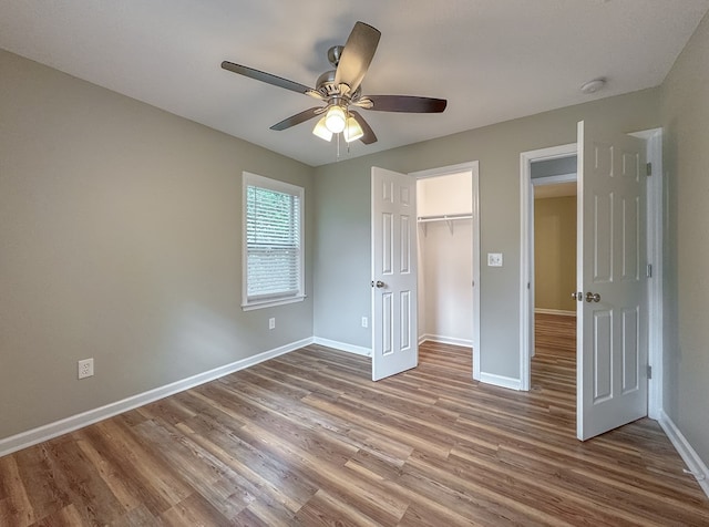 unfurnished bedroom with a walk in closet, a closet, hardwood / wood-style flooring, and ceiling fan