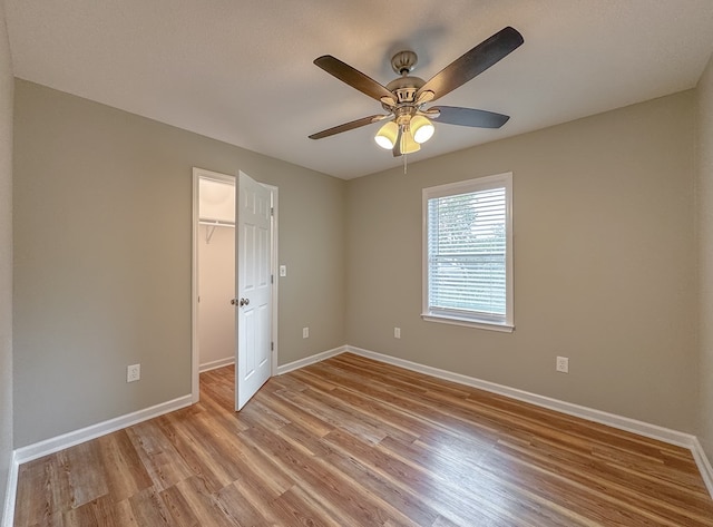 unfurnished bedroom featuring ceiling fan, a closet, a spacious closet, and light hardwood / wood-style flooring