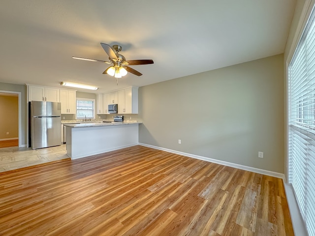 kitchen with white cabinetry, ceiling fan, stainless steel appliances, light hardwood / wood-style flooring, and kitchen peninsula