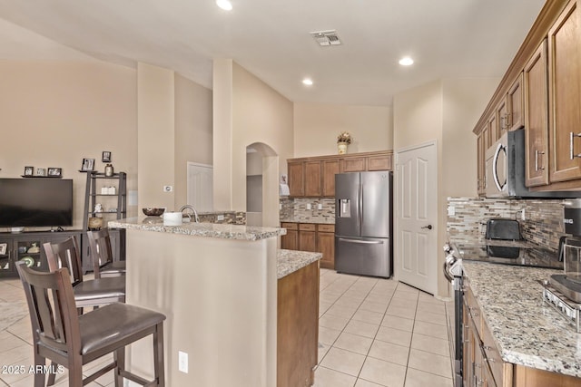 kitchen with light tile patterned floors, visible vents, stainless steel appliances, a kitchen breakfast bar, and brown cabinets