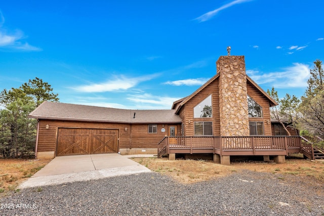 view of front of home featuring a chimney, an attached garage, faux log siding, driveway, and a wooden deck