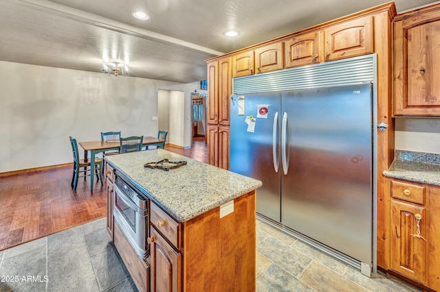 kitchen with light stone counters, a center island, stainless steel built in refrigerator, and baseboards