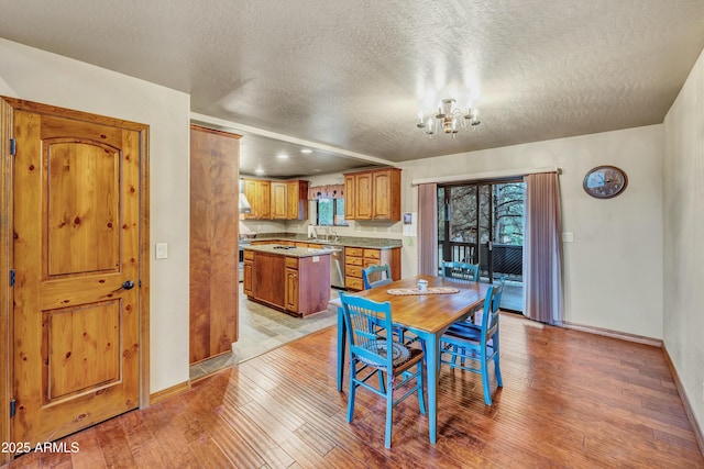 dining area with a chandelier, light wood-type flooring, a textured ceiling, and baseboards