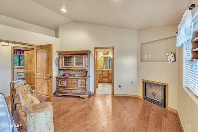 interior space featuring a glass covered fireplace, baseboards, vaulted ceiling, and light wood finished floors