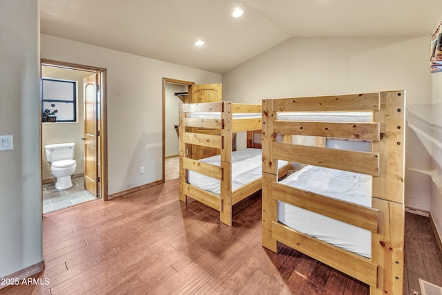 bedroom featuring visible vents, baseboards, lofted ceiling, wood-type flooring, and ensuite bathroom