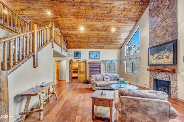 living area featuring high vaulted ceiling, a stone fireplace, wood finished floors, wood ceiling, and stairs