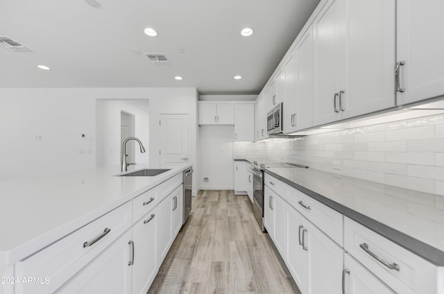 kitchen with light wood-type flooring, sink, white cabinetry, decorative backsplash, and appliances with stainless steel finishes