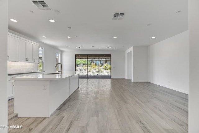 kitchen featuring an island with sink, white cabinets, and light wood-type flooring