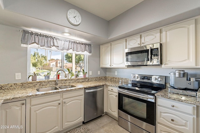 kitchen with light stone countertops, stainless steel appliances, white cabinetry, and sink