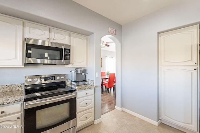 kitchen with ceiling fan, light stone counters, light tile patterned floors, and stainless steel appliances