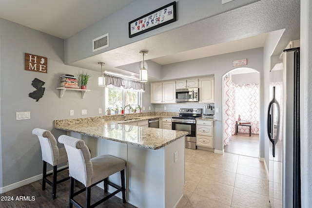 kitchen featuring a kitchen breakfast bar, sink, appliances with stainless steel finishes, decorative light fixtures, and kitchen peninsula