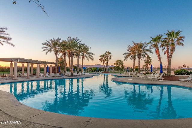 pool at dusk featuring a pergola and a patio