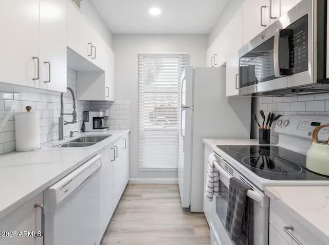 kitchen with sink, white cabinetry, light stone counters, white appliances, and light hardwood / wood-style floors