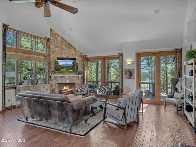 living area featuring high vaulted ceiling, hardwood / wood-style flooring, ceiling fan, and a fireplace
