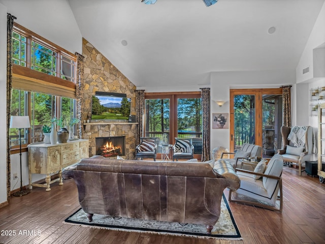 living area featuring high vaulted ceiling, a stone fireplace, and wood-type flooring