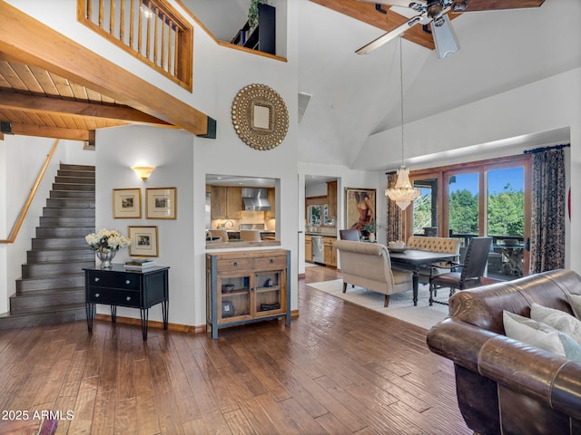 living area with stairs, beamed ceiling, ceiling fan with notable chandelier, high vaulted ceiling, and dark wood-type flooring