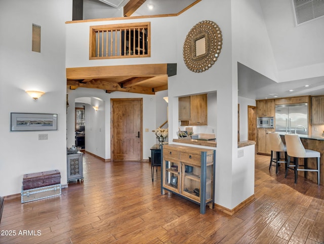 interior space featuring arched walkways, beamed ceiling, baseboards, visible vents, and a high ceiling