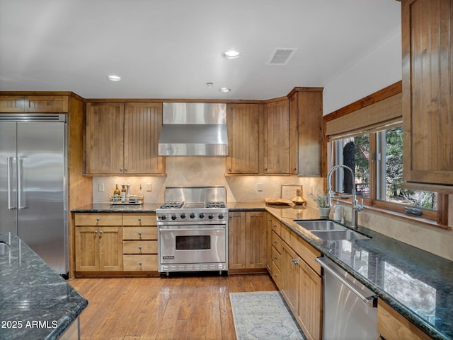 kitchen featuring light wood finished floors, a sink, visible vents, premium appliances, and wall chimney exhaust hood