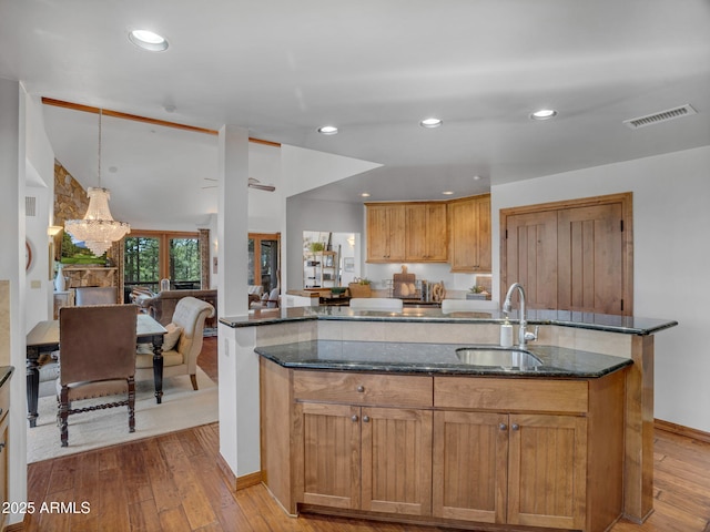 kitchen with dark stone counters, light wood-style floors, a sink, visible vents, and a center island with sink