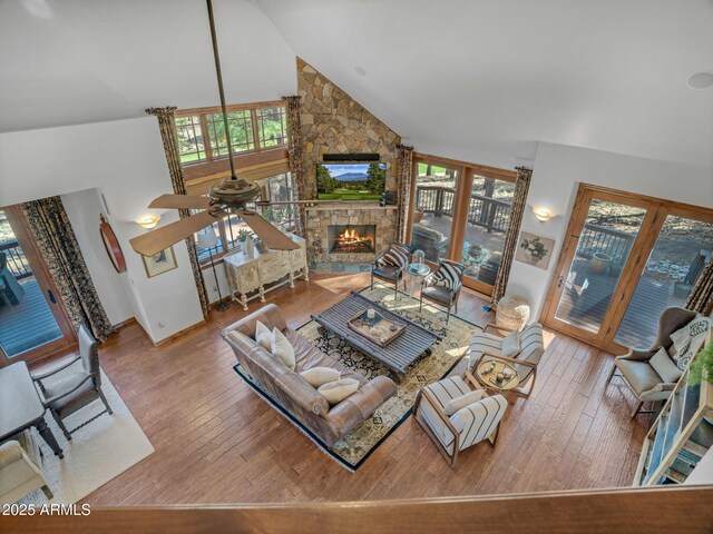living area featuring a stone fireplace, ceiling fan, wood finished floors, and high vaulted ceiling