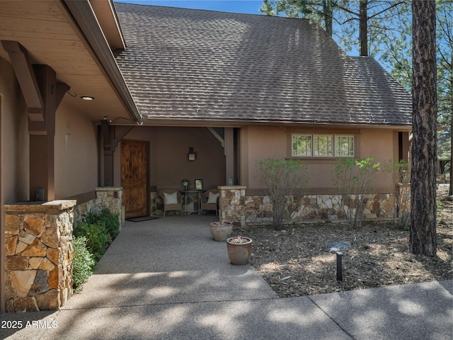 view of front of home with a patio, stone siding, stucco siding, and roof with shingles