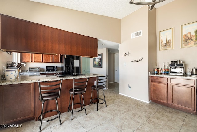 17802 N 45th Ave, Glendale, AZ 85308 - kitchen featuring a kitchen bar, visible vents, light stone countertops, black appliances, and a peninsula