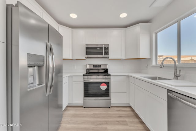 kitchen with white cabinets, light wood-type flooring, stainless steel appliances, and sink