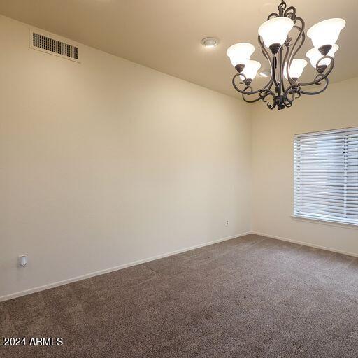 carpeted empty room featuring a notable chandelier