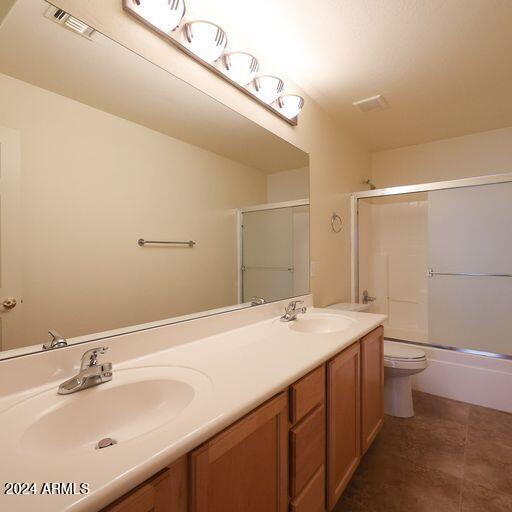 full bathroom featuring shower / bath combination with glass door, tile patterned floors, vanity, and toilet