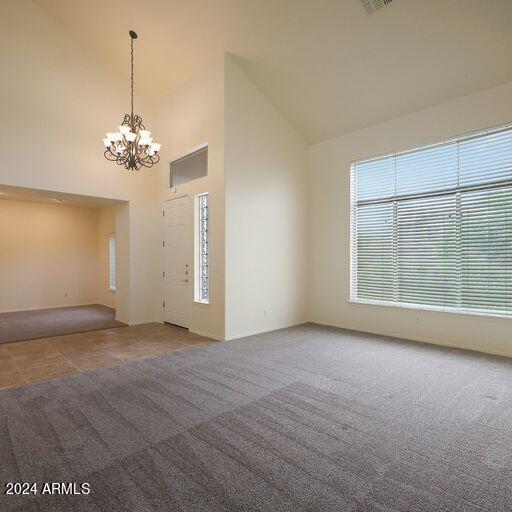 carpeted empty room featuring high vaulted ceiling and a chandelier