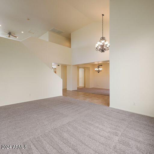 carpeted empty room featuring ceiling fan with notable chandelier and high vaulted ceiling