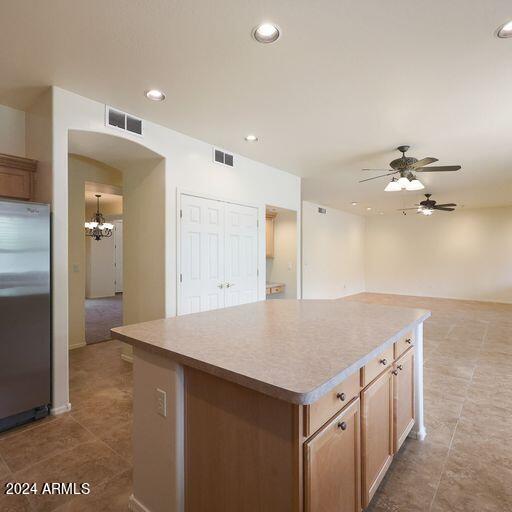 kitchen featuring stainless steel fridge, light tile patterned floors, a kitchen island, and ceiling fan with notable chandelier