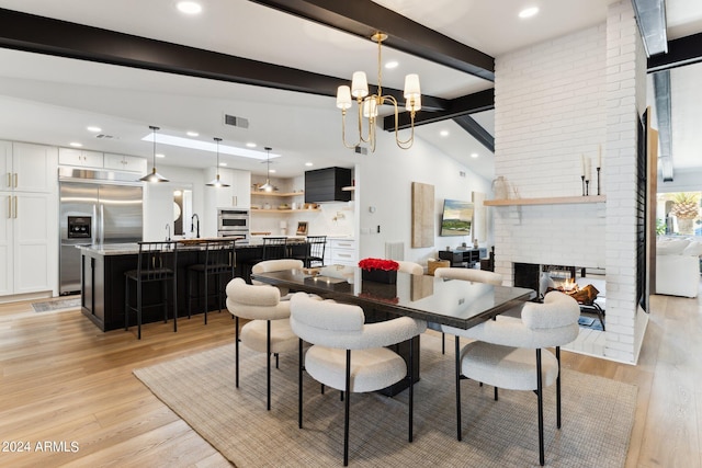 dining area featuring a notable chandelier, a fireplace, vaulted ceiling with beams, and light hardwood / wood-style flooring