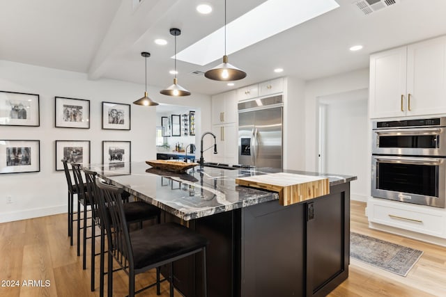 kitchen with dark stone countertops, light hardwood / wood-style floors, appliances with stainless steel finishes, and white cabinetry