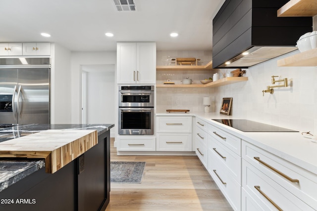 kitchen featuring light wood-type flooring, tasteful backsplash, stainless steel appliances, premium range hood, and white cabinetry