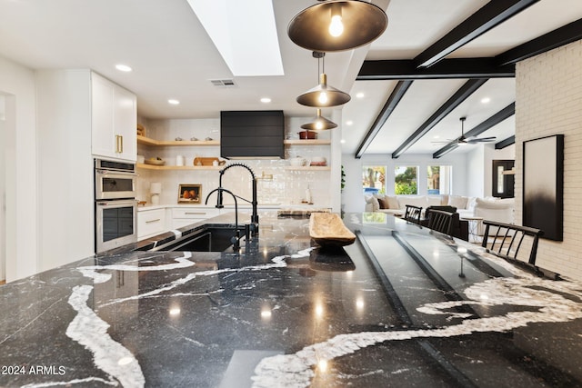 kitchen featuring beam ceiling, decorative light fixtures, white cabinetry, dark stone countertops, and decorative backsplash