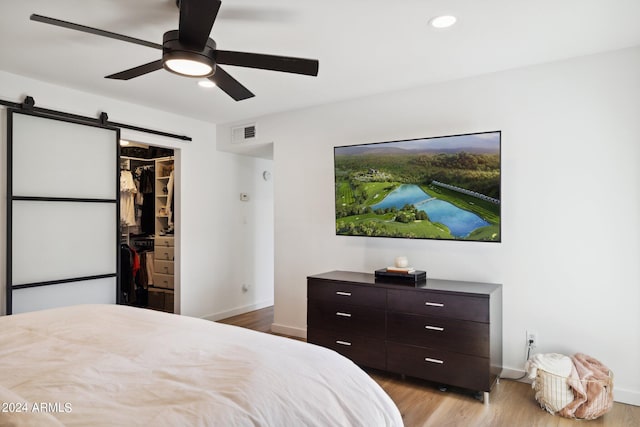 bedroom featuring ceiling fan, a walk in closet, a closet, light wood-type flooring, and a barn door