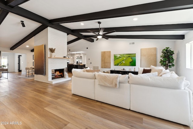 living room with ceiling fan, a brick fireplace, vaulted ceiling with beams, and light hardwood / wood-style flooring