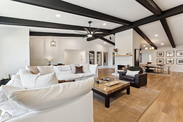 living room with ceiling fan with notable chandelier, a brick fireplace, light hardwood / wood-style floors, and lofted ceiling with beams