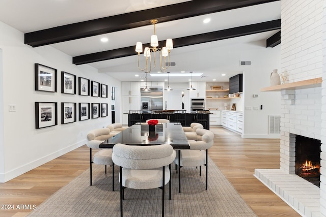 dining area with a brick fireplace, a chandelier, lofted ceiling with beams, and light hardwood / wood-style flooring