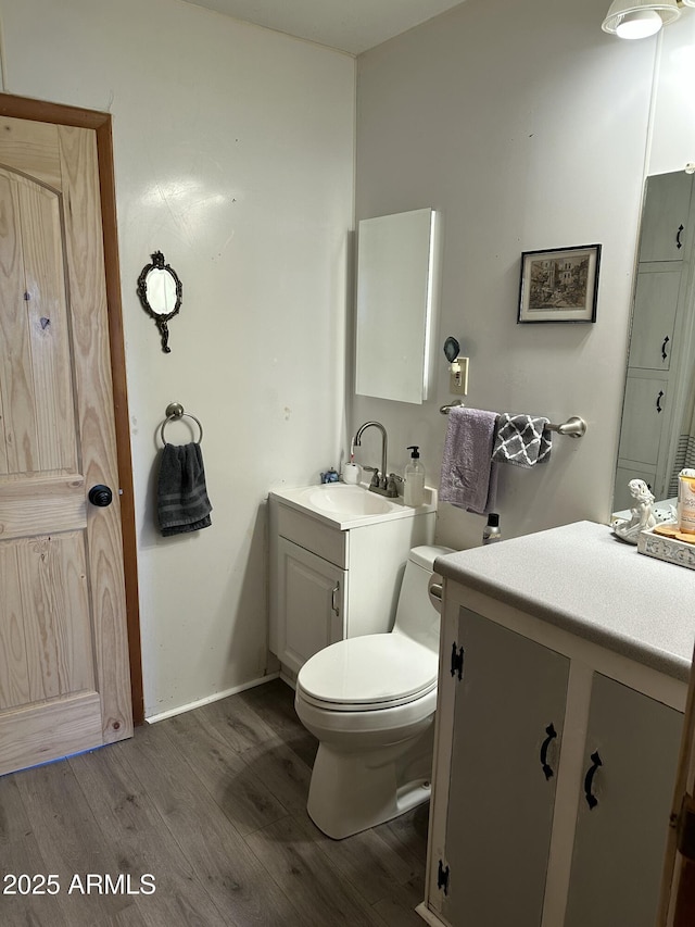 half bath with toilet, baseboards, wood finished floors, and vanity