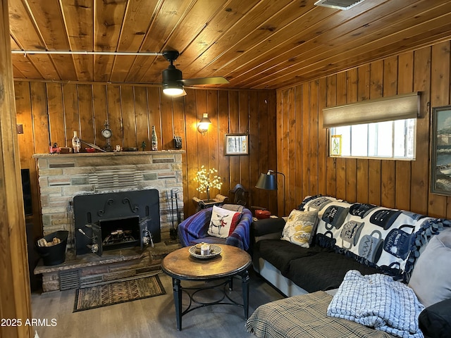 living area with ceiling fan, a stone fireplace, wood walls, wood finished floors, and wood ceiling