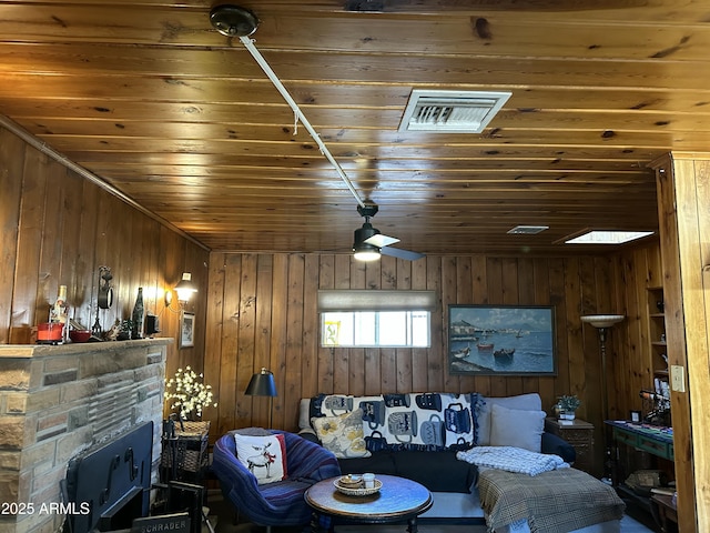 living area featuring wooden ceiling, visible vents, wood walls, and a stone fireplace