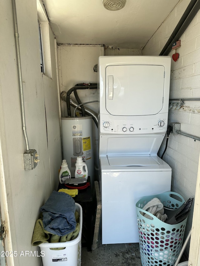 laundry room featuring concrete block wall, stacked washer and dryer, water heater, and laundry area