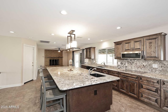 kitchen featuring a fireplace, light stone countertops, a center island with sink, black electric cooktop, and decorative light fixtures