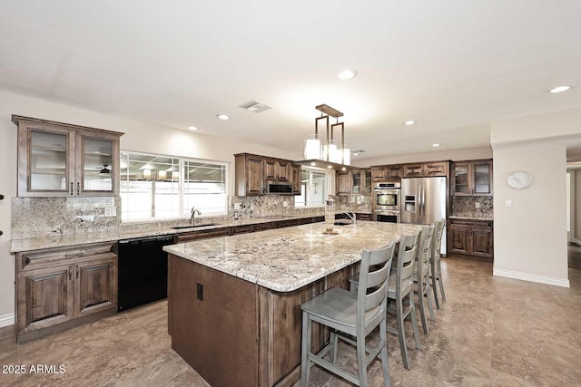 kitchen featuring sink, light stone counters, decorative light fixtures, a large island with sink, and stainless steel appliances